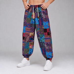 May include: Loose-fitting trousers featuring a vibrant patchwork design with various blue, purple, red, and green geometric and paisley patterns. The pants have an elasticized waistband with white drawstring cords and small colorful beads at the ends.
