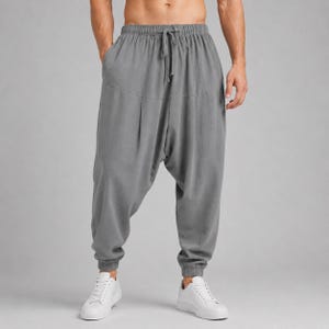 Op de afbeelding: Effen grijze broek met een verlaagd kruis, voorzien van een hoge elastische tailleband met een functioneel trekkoord en elastische boorden bij de enkels. De broek heeft een ruime, losse pasvorm bij de benen en heupen.