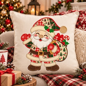May include: A square off-white throw pillow featuring an embroidered Santa Claus graphic. Santa wears a plaid hat and coat with a brown belt, holding a sack filled with gifts and a candy cane. The design includes red, green, and brown colors.