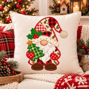 May include: A square off-white throw pillow featuring an embroidered gnome design. The gnome wears a red and black buffalo plaid hat with holly accents, holds a green plaid Christmas tree with a gold star, and has a white beard and brown shoes.