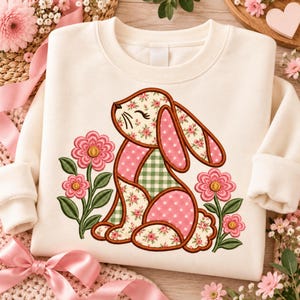 May include: A cream-colored sweatshirt featuring a central embroidered graphic of a rabbit composed of patchwork-style patterns including pink floral, pink polka dot, and green gingham prints, flanked by two pink flowers with green stems.
