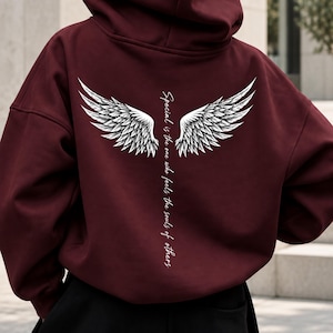 Puede incluir: Una sudadera con capucha de color burdeos oscuro que presenta un gráfico blanco en la espalda. El diseño muestra dos alas de ángel detalladas sobre un texto vertical blanco que dice, Special is the one who feels the souls of others.