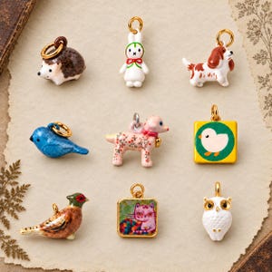 May include: A collection of nine small animal-themed charms featuring a hedgehog, a white rabbit, a brown and white dog, a blue bird, a pink floral dog, a yellow square with a chick, a pheasant, a square cat portrait, and a white owl.