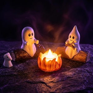 Peut inclure: Deux figurines de fantômes blancs avec des yeux et des bouches noirs sont assises sur des bûches brunes texturées. Entre elles se trouve une petite lumière orange en forme de flamme. Un minuscule fantôme blanc se tient à gauche.
