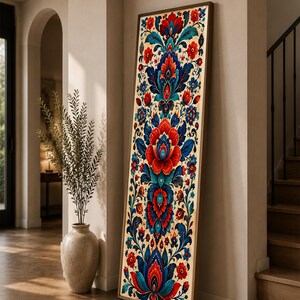 Può includere: Un'opera d'arte da parete alta e rettangolare con cornice, caratterizzata da un motivo floreale simmetrico in vivaci tonalità di rosso, blu intenso e verde acqua su sfondo crema, disposta verticalmente con una sottile cornice in legno.