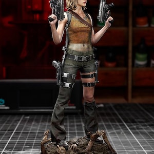 Peut inclure: Une figurine de collection représentant un personnage aux cheveux bruns mi-longs, portant un haut en maille orange, un pantalon sombre et une ceinture avec des étuis. La figurine tient deux pistolets noirs et repose sur un socle avec des mains sculptées.