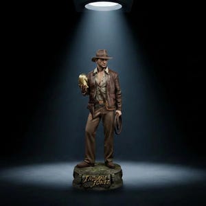 May include: A detailed figurine of Indiana Jones wearing a brown fedora, a leather jacket, and tan trousers. The figure holds a golden idol in one hand and a coiled whip in the other, standing on a base with the text Indiana Jones engraved on it.