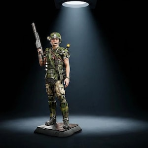 Könnte beinhalten: Eine detaillierte Sammlerfigur eines Soldaten in taktischer Tarnkleidung, der einen Helm mit montierter Lampe trägt, ein Gewehr in der rechten Hand hält und auf einem quadratischen Sockel unter einem Scheinwerfer vor dunklem Hintergrund steht.