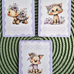 Op de afbeelding: Drie rechthoekige kaarten met geschulpte randen en een lichtpaarse omlijsting. Elke kaart toont een centrale illustratie van een klein dier—een schildpad, een kitten of een puppy—versierd met paarse bloemen. Boven en onder staan vijf lege cirkels.
