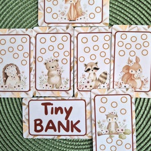 Op de afbeelding: Een verzameling rechthoekige kaarten met illustraties van een vos, egel, beer, wasbeer, eekhoorn en uil, elk versierd met bloemenkransen. De kaarten bevatten cirkelvormige contouren en één kaart toont de tekst Tiny BANK.
