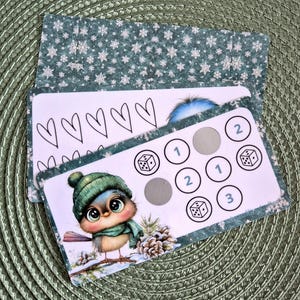 Op de afbeelding: Een rechthoekige spelkaart met een lichtroze achtergrond en een getekende vogel met een groene gebreide muts en sjaal. De kaart bevat gedrukte cirkels met de cijfers één, twee en drie, dobbelsteeniconen en grijze krasvlakken om open te krassen.
