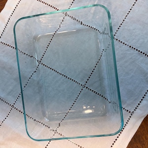 Puede incluir: Una fuente de horno rectangular de cristal transparente con esquinas redondeadas y paredes lisas. El recipiente presenta un interior profundo y abierto con una base plana, diseñado para su uso en el horno, con una estructura sencilla.