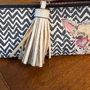 Puede incluir: Dos neceseres con cremallera. Una bolsa presenta un patr&oacute;n de chevr&oacute;n en blanco y negro, la otra tiene un chihuahua con gafas de sol en forma de coraz&oacute;n. Ambas bolsas tienen una borla beige adjunta a la cremallera.