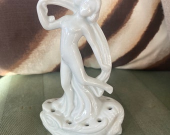 May include: White porcelain figurine of a woman with flowing drapery, standing on a base with holes for flower stems. The figurine is a vintage style.