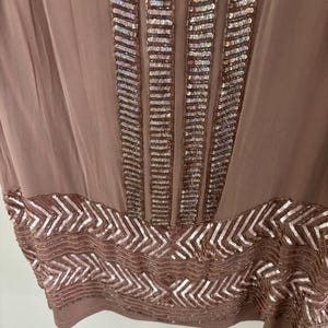Peut inclure: Une robe de couleur mauve avec des d&eacute;tails de sequins complexes. Des colonnes verticales de sequins ornent le corsage, tandis qu'un motif en chevrons de sequins d&eacute;core l'ourlet. La robe est faite d'un tissu fluide et l&eacute;ger.