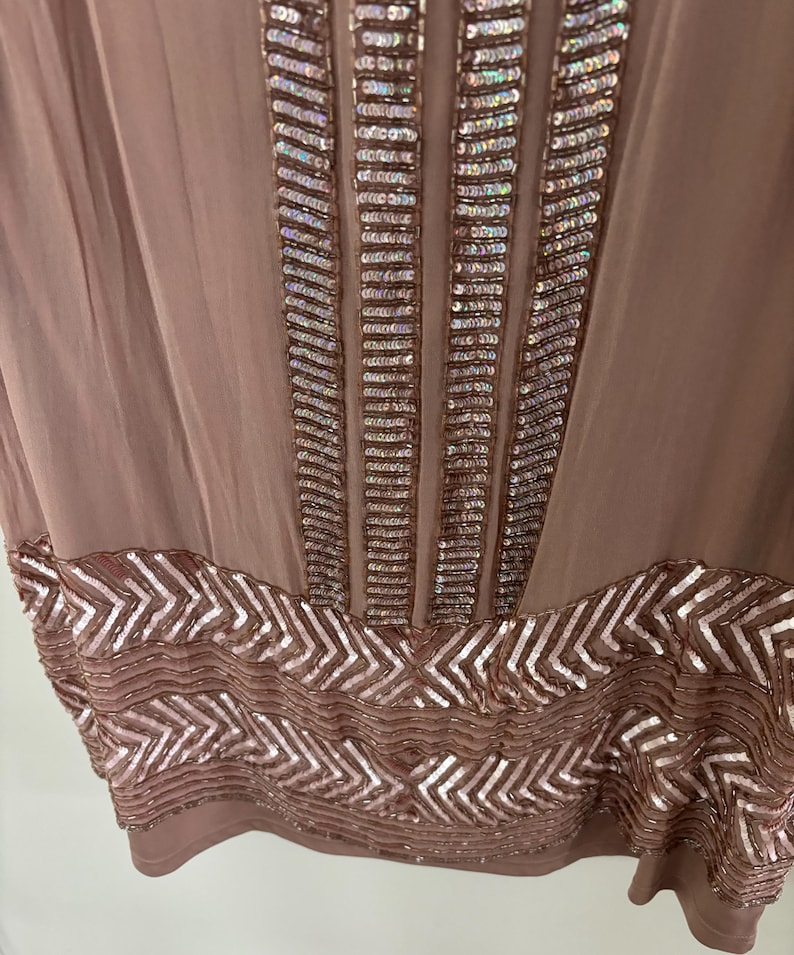 Peut inclure: Une robe de couleur mauve avec des d&eacute;tails de sequins complexes. Des colonnes verticales de sequins ornent le corsage, tandis qu'un motif en chevrons de sequins d&eacute;core l'ourlet. La robe est faite d'un tissu fluide et l&eacute;ger.