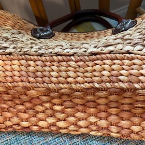 Puede incluir: Bolso tote de paja tejida con asas de cuero marr&oacute;n y detalles decorativos. El bolso presenta una paleta de colores naturales con un dise&ntilde;o tejido apretado, mostrando una estructura robusta y espaciosa. El bolso est&aacute; dise&ntilde;ado para transportar objetos.