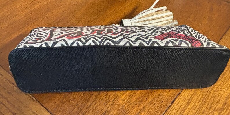 Puede incluir: Bolso de mano rectangular con base negra y estampado en zigzag blanco y negro. La palabra "love" est&aacute; escrita en rojo. El bolso tiene una borla.