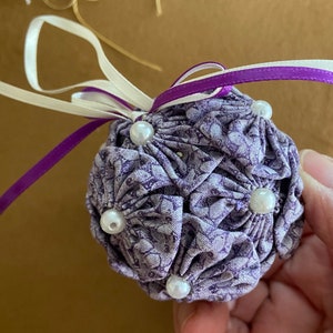May include: A purple fabric Christmas bauble with white pearl beads and a white and purple ribbon.