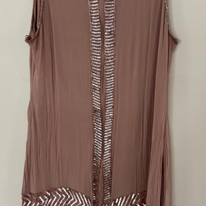 Peut inclure: Robe sans manches de couleur mauve avec des d&eacute;tails de sequins. La robe pr&eacute;sente un col orn&eacute; de sequins, une bande verticale de sequins au centre et un motif en chevrons &agrave; l'ourlet. Suspendue &agrave; un cintre noir.