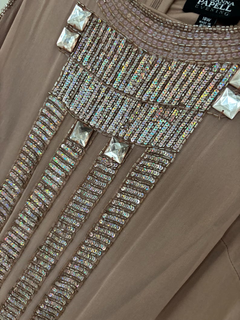 Peut inclure: Robe de soir&eacute;e taupe avec des ornements complexes de sequins et de perles. L'encolure et le haut du corsage pr&eacute;sentent des rang&eacute;es de petits sequins iris&eacute;s et de plus gros cristaux carr&eacute;s et transparents. La robe est &eacute;tiquet&eacute;e "ANNA PAPELL EVENING" et taille 18W.