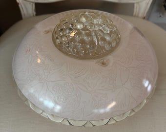 May include: A vintage light fixture with a pale pink, floral-patterned shade. The shade has a scalloped edge and a clear, textured glass center. The fixture is likely from the mid-century era and is sitting on a white surface.