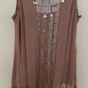 Peut inclure: Robe sans manches de couleur mauve orn&eacute;e de sequins et de perles. La robe pr&eacute;sente un d&eacute;collet&eacute; perl&eacute;, des motifs g&eacute;om&eacute;triques et des lignes verticales de sequins. La marque "Adrianna Papell" est visible sur l'&eacute;tiquette.