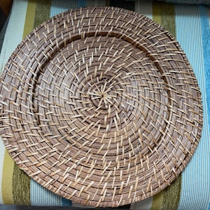 May include: A round, woven placemat in shades of brown. The placemat has a spiral design, with the weave radiating from the center. The texture is visible, showing the individual strands of material. This decorative piece is suitable for dining and home decor.