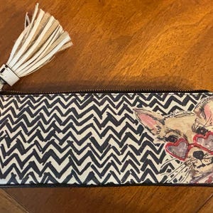 Puede incluir: Estuche rectangular con un patr&oacute;n de chevr&oacute;n en blanco y negro. El estuche tiene cierre de cremallera y una borla color crema. Un dibujo de un chihuahua con gafas de sol en forma de coraz&oacute;n est&aacute; impreso en la parte delantera.