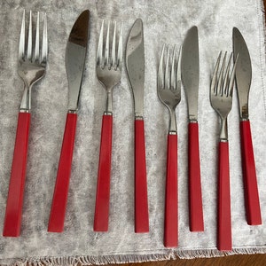 May include: Set of eight red-handled silverware, including a knife, forks, and spoons. The silverware has a polished silver finish.