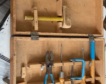 May include: A wooden toolbox with a variety of tools, including a hammer, pliers, a screwdriver, a clamp, and a ruler. The tools are all in their designated slots in the toolbox.