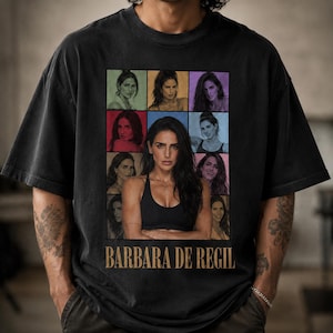 May include: A black short-sleeve t-shirt featuring a central graphic collage of multiple portraits of Barbara de Regil. The design includes a larger central image of the subject in a black sports bra, surrounded by smaller framed photos, with the text BARBARA DE REGIL printed in a bold, tan-colored serif font at the bottom.