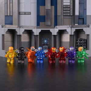 Könnte beinhalten: Acht kleine Kunststoff-Actionfiguren stehen in einer Reihe, jede trägt eine andersfarbige, durchscheinende Rüstung mit flügelartigen Aufsätzen. Die Figuren sind gelb, schwarz, orange, blau, rot, dunkelrot, lila und grün gefärbt.