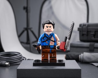 Puede incluir: Una minifigura de plástico con cabello negro, camisa azul con arnés negro y pantalones marrones. La figura tiene una motosierra roja en una mano y un arma de fuego negra en la otra, con detalles impresos que muestran ropa desgarrada.