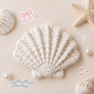 May include: A cream-colored crocheted seashell with a ribbed texture. The shell is surrounded by a natural white seashell, a tan starfish, two white pearls, and graphic illustrations of a pink bow, small hearts, and blue wavy lines.