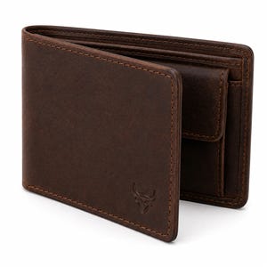 Puede incluir: Una cartera bifold de cuero marrón oscuro con un acabado mate suave y costuras visibles a lo largo de los bordes. El exterior frontal muestra un pequeño logotipo de toro en relieve en la esquina inferior derecha y el interior incluye un monedero.