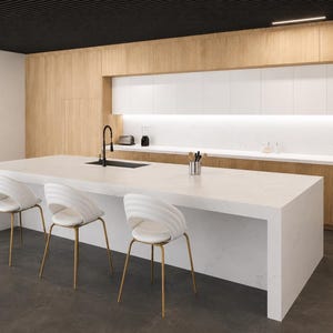 Peut inclure: Un îlot de cuisine avec un comptoir blanc et trois chaises blanches aux pieds dorés. La cuisine présente des armoires en bois clair, des placards blancs, un robinet noir et un sol gris foncé. L'agencement est linéaire et épuré.
