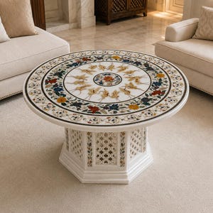 Puede incluir: Una mesa de centro redonda de mármol blanco con un intrincado patrón incrustado de flores y aves en la superficie superior. La base es octogonal con paneles de celosía tallados e incrustaciones florales que sostienen la mesa.