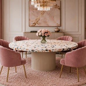 May include: A round dining table with a white terrazzo top and a beige fluted cylindrical base, surrounded by six pink velvet upholstered chairs with gold metal legs, arranged on a round pink shag rug in a dining room setting.