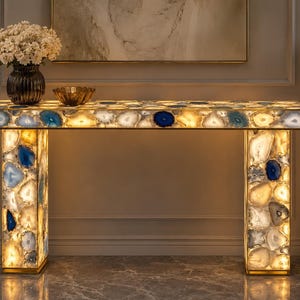 May include: A rectangular console table constructed from backlit agate slices in shades of blue, white, and amber. The table features a flat top and two vertical pillar legs, all illuminated from within to highlight the natural stone patterns.