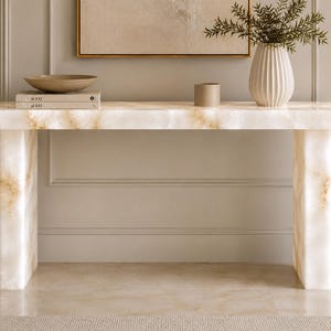 May include: A rectangular console table crafted from white and cream-colored stone with natural golden-brown veining. The table features a smooth, flat top supported by two thick, solid rectangular legs, showcasing a polished, translucent finish.