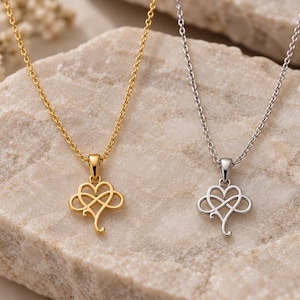 May include: Two necklaces with delicate chains, one in gold tone and one in silver tone. Each pendant features a combined heart and infinity symbol design with a smooth, polished finish. The pendants hang from matching metal link chains.