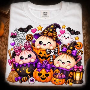May include: A white t-shirt featuring a colorful graphic of three cute dumpling characters in Halloween costumes. The design includes pumpkins, a witch hat, a broom, a lantern, bats, spiders, candy, and hearts, with the Comfort Colors brand label.