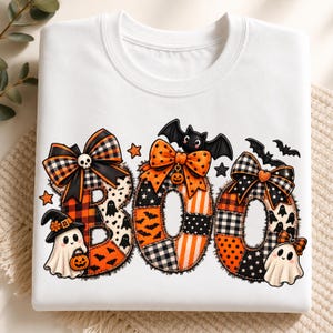 May include: A white crewneck sweatshirt featuring the word BOO in large letters. Each letter is filled with orange, black, and white patterns including plaid, polka dots, and bats. The letters are decorated with bows, ghosts, and bats.