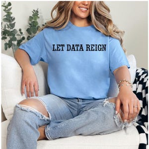 Könnte beinhalten: Ein hellblaues Kurzarm-T-Shirt mit dem schwarzen Schriftzug LET DATA REIGN, der in einer fetten, abgenutzten Serifenschrift mittig auf der Brust gedruckt ist. Das Shirt hat einen Rundhalsausschnitt und eine normale Passform aus einfarbigem Stoff.