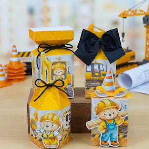 May include: Four yellow and white construction-themed favor boxes featuring illustrations of teddy bears in hard hats. Two boxes are topped with black bows, while the others have black string ties. The designs include yellow diamond patterns and construction vehicle graphics.