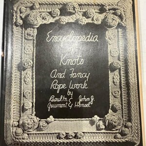 May include: A black and white hardcover book titled Encyclopedia of Knots and Fancy Rope Work by Raoul M. Graumont and John J. Hensel. The cover features a decorative border of rope knots and the text Fourth Edition, 420 New Examples, 31 New Plates.