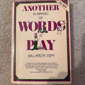 May include: A paperback book titled Another Almanac of Words at Play by Willard R. Espy. The cover features purple text, a small illustration of a figure in a top hat, a dog, and a banner in the corner that reads ALL NEW. A quote is printed at the bottom.