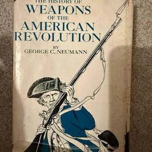 May include: A hardcover book titled The History of Weapons of the American Revolution by George C. Neumann. The cover features a black and white line drawing of a soldier in a tricorn hat holding a long musket with a bayonet, wearing a blue coat.