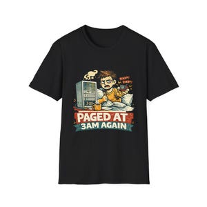 May include: A black short-sleeve t-shirt featuring a graphic of a person in bed with a server tower and a coffee mug. The text reads BEEP BEEP and PAGED AT 3AM AGAIN. The illustration shows a frustrated person holding a pager in a bedroom setting.
